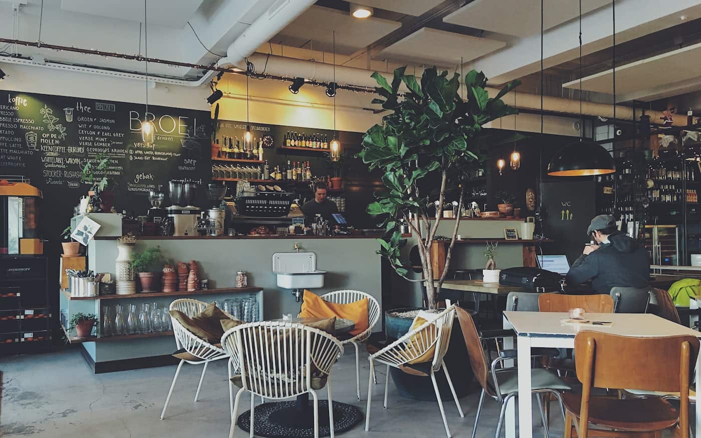 Bright cafe interior with people at marble tables and a long counter in the early morning