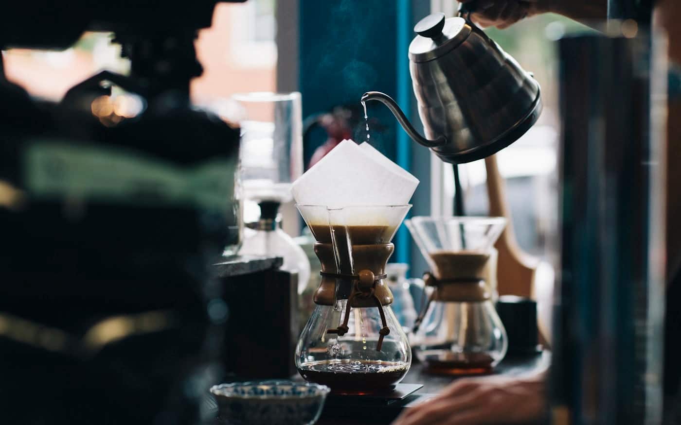 Water pouring from a gooseneck kettle onto coffee grounds in a V60 dripper sitting on a brew scale