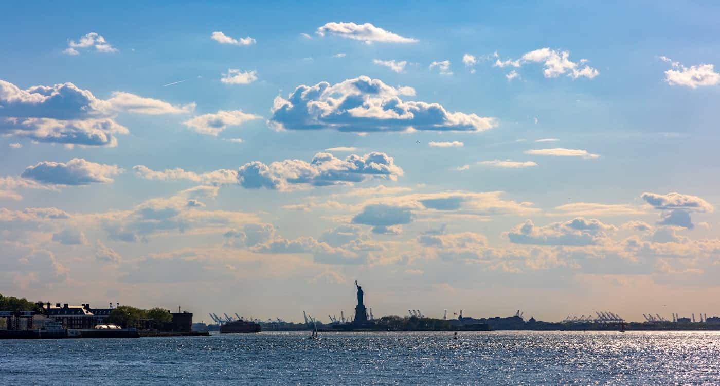Harbor view from south Brooklyn with the Statue of Liberty on the horizon under scattered clouds